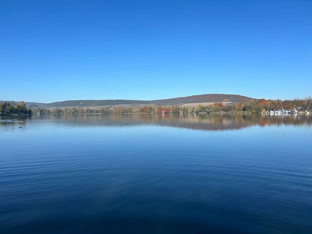 Ein See liegt vor uns, der Himmel ist strahlend blau, am Horizont sieht man ein paar Bäume und Vegetation.