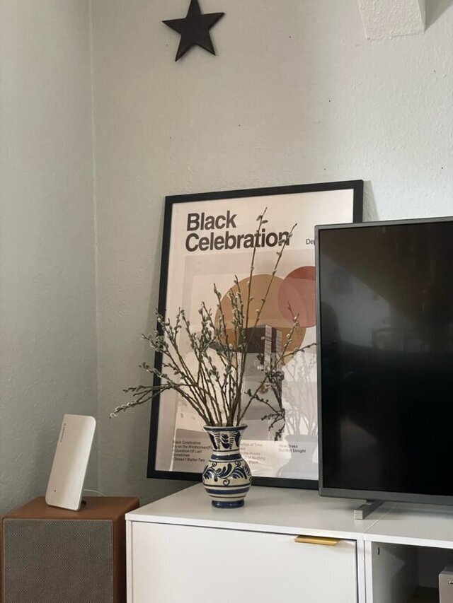 Ein Bild steht auf einem Board, mittig eine Blumenvase mit Zweigen.
