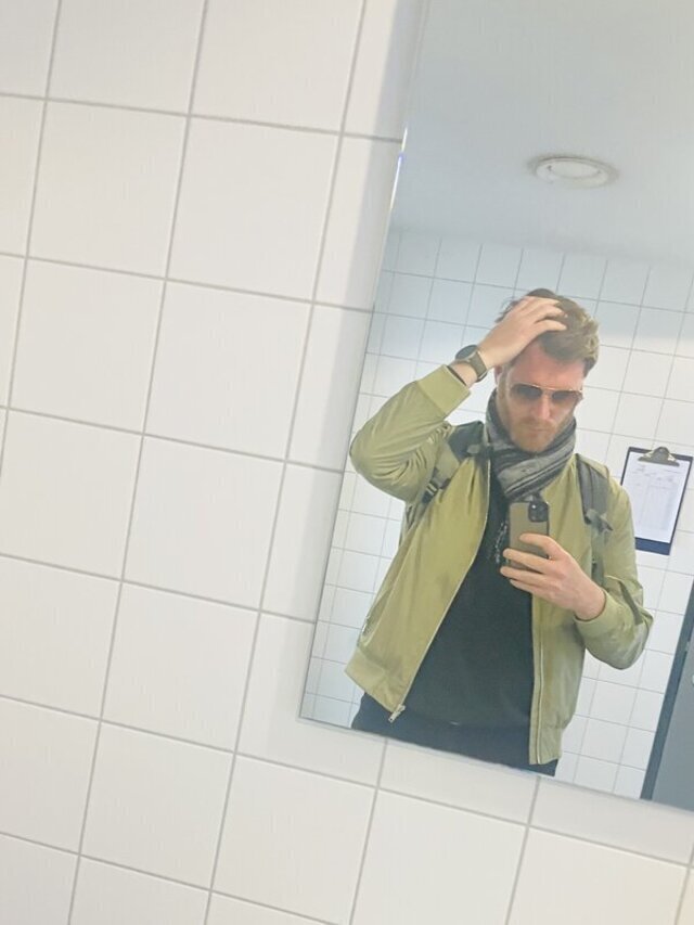 Herr Montag trägt eine grüne bomberjackenähnliche Jacke und einen Schal. Der Raum ist gefliest.