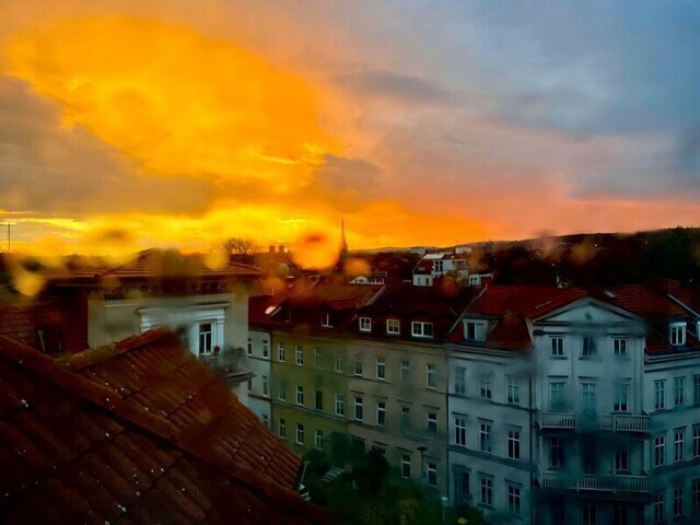 Ein regennasses Fenster und der Blick in über die Stadt in den Himmel, es leuchtet Bernstein