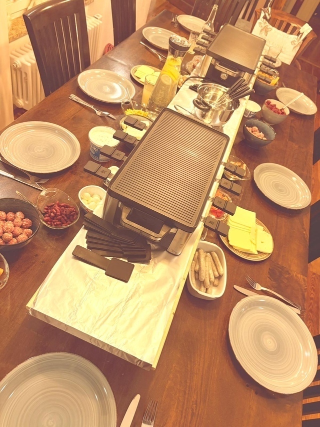 Raclette, zwei, auf einem langen Tisch, eine Art Tafel. Allerlei Unrat hier und dort.