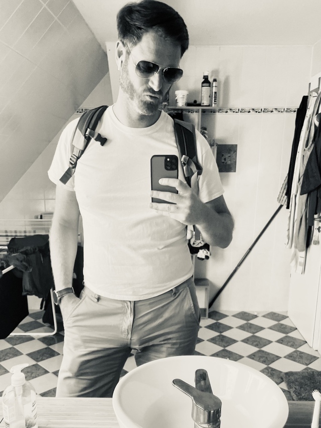 Herr Montag in weißen T-Shirt und Rucksack posiert vor einem Spiegel